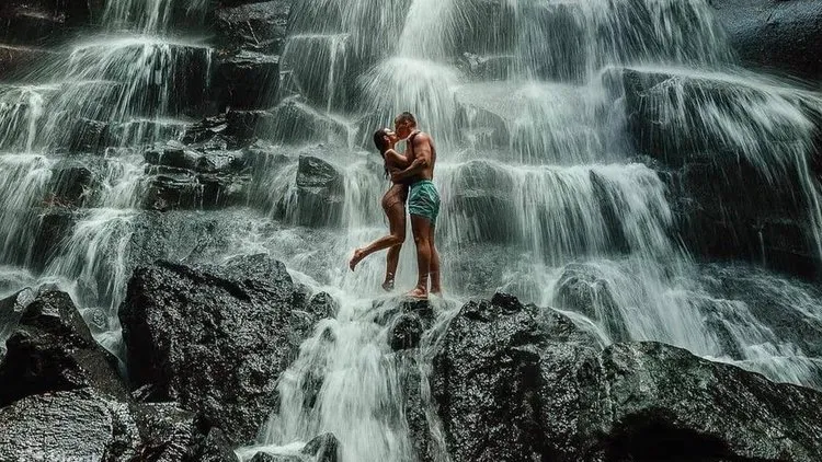Couple standing in the spray at Kanto Lampo Waterfall in Bali near Ubud with tiered black volcanic rock cascade behind them
