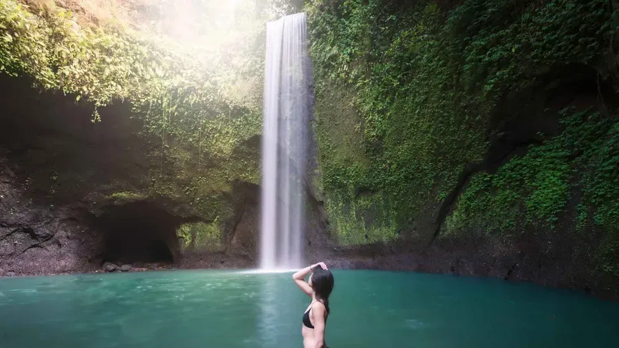 Single curtain of Tibumana waterfall falling into a calm swimmable pool in a quiet jungle valley near Ubud Bali