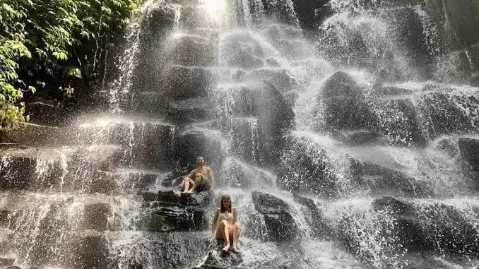 Tourists photographing the stepped curtain of Kanto Lampo Waterfall in Bali near Ubud with tropical vegetation along the rocky cliff